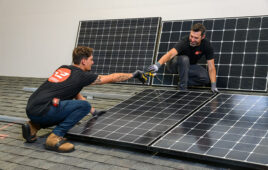 Two people crouch on a section of rooftop used for training modules and demonstrate how to install solar panels.
